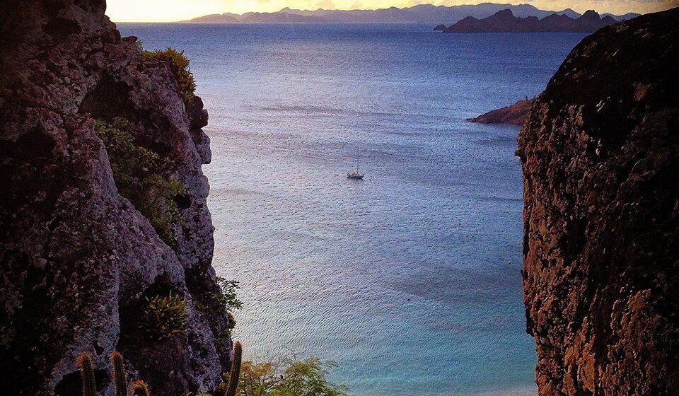 Une belle vue sur l'océan encadré de rochers avec un bateau naviguant au loin, entouré d'eaux calmes.